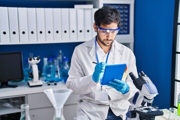 Young hispanic man scientist using touchpad at laboratory