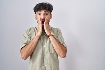 Arab man with beard standing over white background afraid and shocked, surprise and amazed expression with hands on face