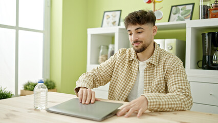 Fototapeta premium Young arab man opening laptop sitting on table at home