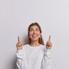 Check out this cool offer. Smiling woman points index fingers overhead shows blank space for your...