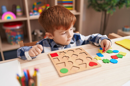 Adorable toddler playing with maths puzzle game sitting on table at classroom