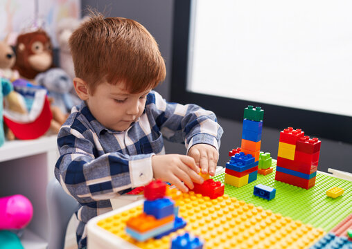 Adorable toddler playing with construction blocks sitting on table at kindergarten