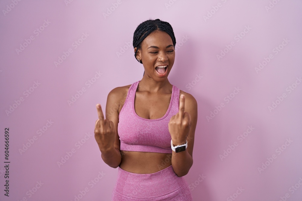 Poster african american woman with braids wearing sportswear over pink background showing middle finger doi