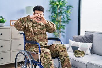 Arab man wearing camouflage army uniform sitting on wheelchair smiling in love doing heart symbol shape with hands. romantic concept.