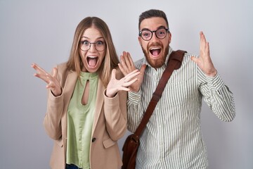 Young couple standing over white background celebrating crazy and amazed for success with arms...