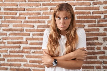 Fototapeta na wymiar Young caucasian woman standing over bricks wall shaking and freezing for winter cold with sad and shock expression on face