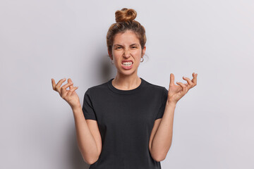 Enraged furious woman clenches teeth and gestures angrily expresses aggressive emotions looks with...