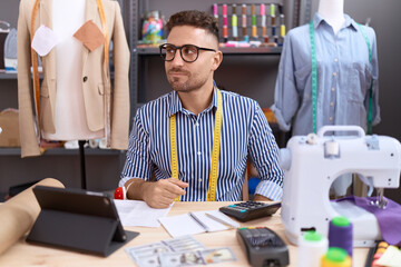 Hispanic man with beard dressmaker designer working at atelier smiling looking to the side and staring away thinking.