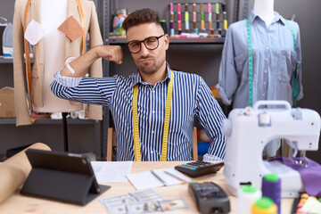 Hispanic man with beard dressmaker designer working at atelier strong person showing arm muscle, confident and proud of power