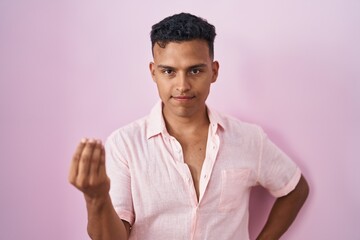 Young hispanic man standing over pink background doing italian gesture with hand and fingers confident expression