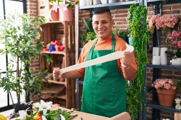 Young latin man florist smiling confident holding gift lace at flower shop