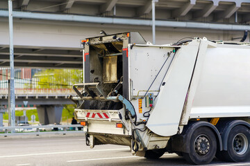 A white car for collecting and transporting garbage is driving along the highway
