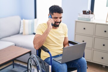 Young arab man talking on smartphone sitting on wheelchair at home