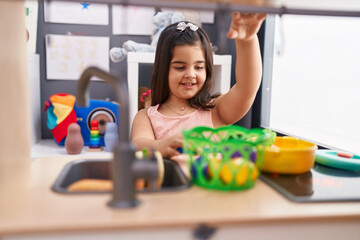 Adorable hispanic girl playing with play kitchen standing at kindergarten