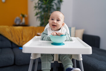 Adorable caucasian baby smiling confident sitting on highchair at home