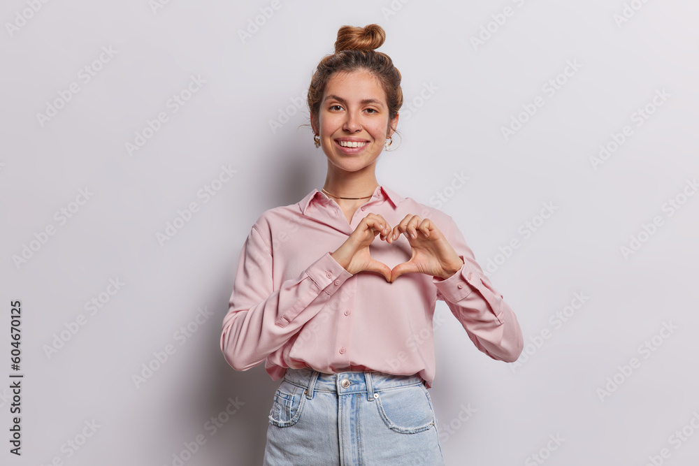 Wall mural beautiful lovely girlfriend likes something shows i love you sign smiles pleasantly dressed in shirt