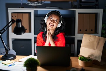 Young asian woman working at the office with laptop at night begging and praying with hands together with hope expression on face very emotional and worried. begging.