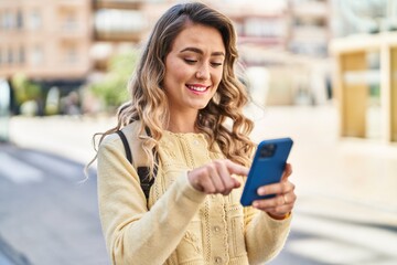 Young woman tourist smiling confident using smartphone at street