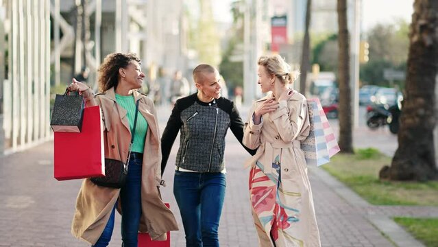 Three cheerful women friends walking with shopping bags in town on street - Female Friendship 