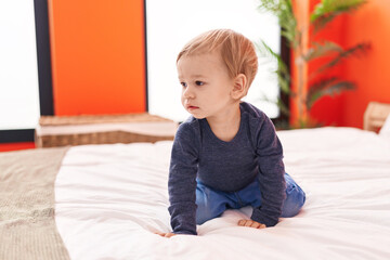 Fototapeta premium Adorable blond toddler sitting on bed with with relaxed expression at bedroom