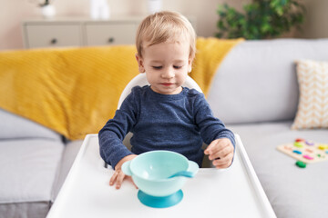 Adorable blond toddler sitting on highchair waiting to eat at home