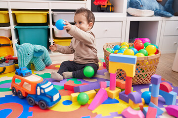 Adorable hispanic boy playing with balls sitting on floor at kindergarten