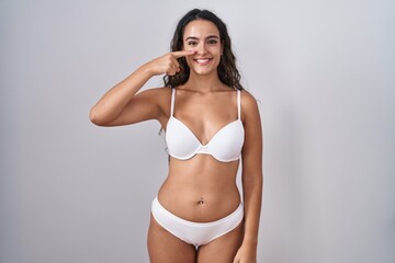 Fototapeta premium Young hispanic woman wearing white lingerie pointing with hand finger to face and nose, smiling cheerful. beauty concept