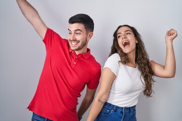 Young hispanic couple standing over isolated background dancing happy and cheerful, smiling moving casual and confident listening to music