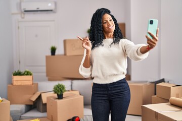Fototapeta na wymiar Middle age hispanic woman moving to a new home taking selfie picture smiling happy pointing with hand and finger to the side