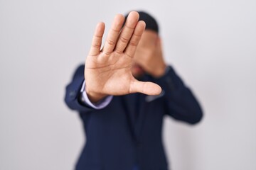 Young hispanic man wearing business suit and tie covering eyes with hands and doing stop gesture with sad and fear expression. embarrassed and negative concept.