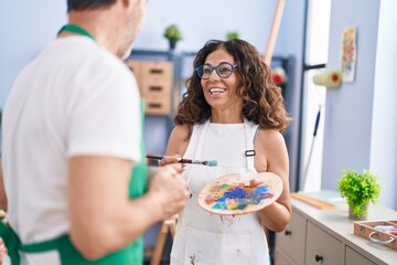 Man and woman artists drinking coffee holding paintbrush and palette at art studio