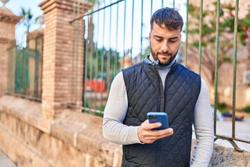 Young hispanic man using smartphone at street