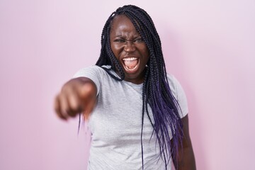 Young african woman standing over pink background pointing displeased and frustrated to the camera,...