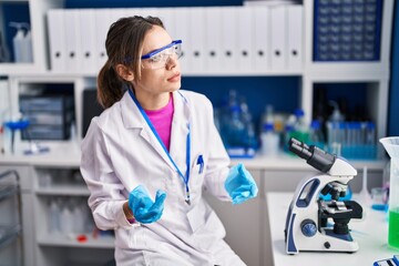 Young beautiful hispanic woman scientist sitting with relaxed expression at laboratory