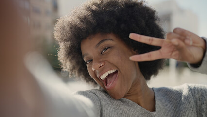 African american woman making selfie by camera doing victory gesture at street