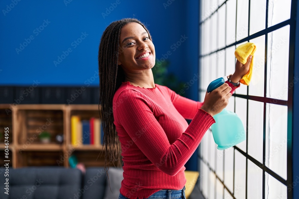 Wall mural African american woman smiling confident cleaning window at home