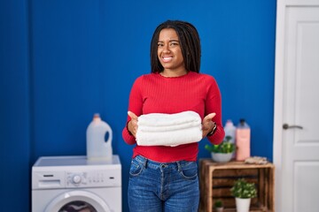 Young african american with braids holding clean laundry clueless and confused expression. doubt concept.