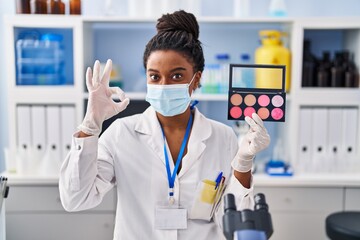 Young african american with braids working at scientist laboratory doing make up doing ok sign with fingers, smiling friendly gesturing excellent symbol