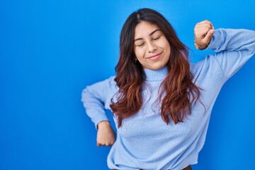 Fototapeta premium Hispanic young woman standing over blue background stretching back, tired and relaxed, sleepy and yawning for early morning