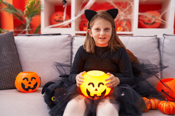 Adorable blonde girl wearing halloween costume holding pumpkin basket at home