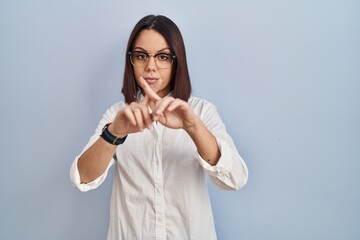 Young hispanic woman standing over white background rejection expression crossing fingers doing negative sign