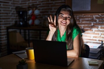 Young teenager girl working at the office at night showing and pointing up with fingers number...