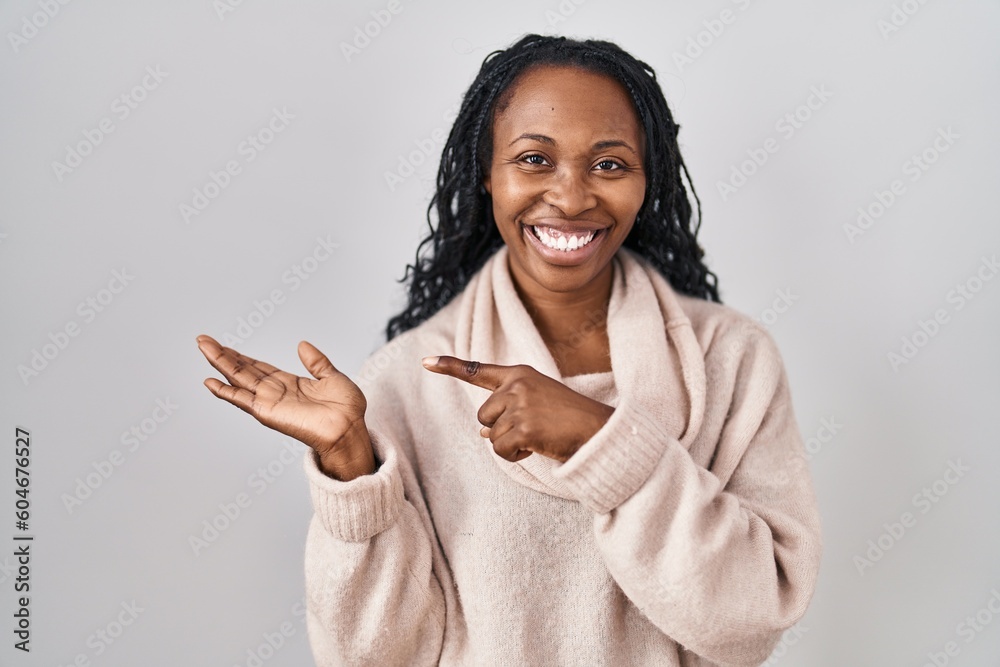 Sticker African woman standing over white background amazed and smiling to the camera while presenting with hand and pointing with finger.