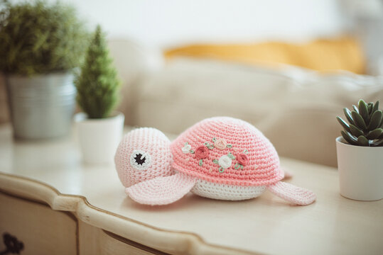 Crochet turtle (Amigurumi ) on a sideboard next to assorted houseplants