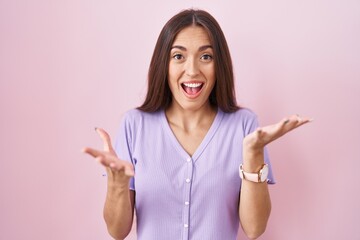 Young hispanic woman with long hair standing over pink background celebrating crazy and amazed for success with arms raised and open eyes screaming excited. winner concept