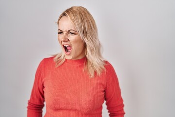 Blonde woman standing over isolated background angry and mad screaming frustrated and furious, shouting with anger. rage and aggressive concept.