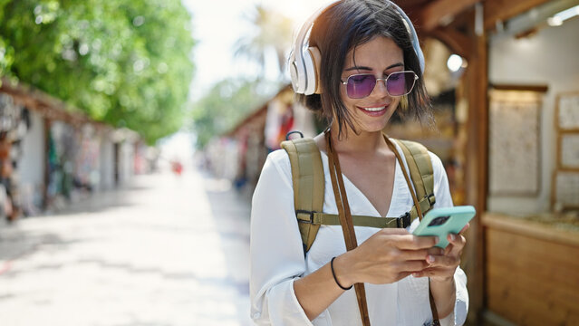 Young beautiful hispanic woman tourist smiling confident listening to music at street market