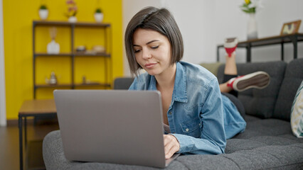 Young caucasian woman using laptop lying on sofa at home