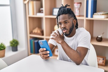 African american woman using smartphone sitting on table at home