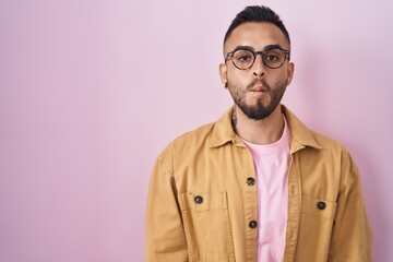 Young hispanic man standing over pink background making fish face with lips, crazy and comical gesture. funny expression.